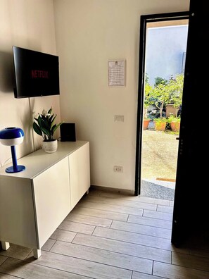 A room with a TV on the wall, a desk with a lamp, a potted plant, and a door leading outside. - Quiet One-Bedroom Apartment 80 m from the M1 Metro (Milano)