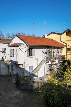 A residential building with a red-tiled roof, a balcony with hanging plants, and a small garden area. - Quiet One-Bedroom Apartment 80 m from the M1 Metro (Milano)
