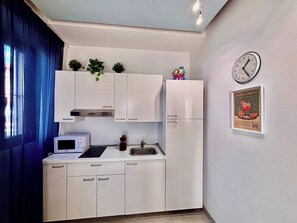 A compact kitchen with white cabinets, a microwave, a sink, and a clock on the wall. - Quiet One-Bedroom Apartment 80 m from the M1 Metro (Milano)