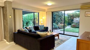 Un salon moderne avec un canapé foncé, une table basse et une vue sur un jardin, visible à travers de grandes portes-fenêtres coulissantes.