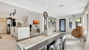 A modern kitchen with a built-in oven, a dining area with a long table, and a living space with a sofa and a TV. - Modern Home • Pool • Near Beach & Las Olas (Fort Lauderdale)