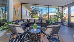 A modern outdoor seating area with a sofa, chairs, and a table, surrounded by large windows and potted plants. - 2 Homes! - 4 MN to Madiera BCH - Hottub - HTD Pool (St. Petersburg)