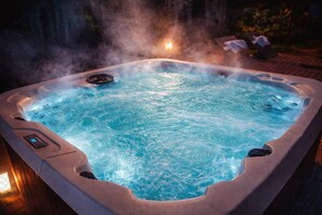 Ein Whirlpool mit aufsteigendem Dampf, umgeben von einer Holzterrasse und einer Kerze.