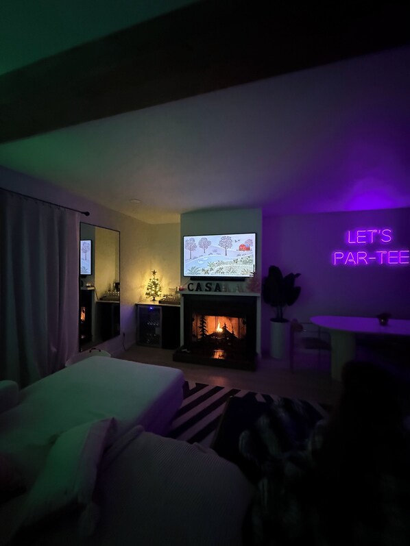 A hotel room with a television, fireplace, and a neon sign on the wall.
