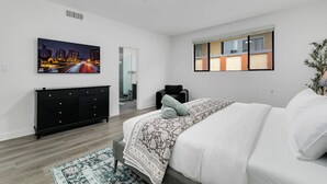 Une chambre à coucher avec un lit, une table de chevet, une commode, une fenêtre et un tableau accroché au mur.