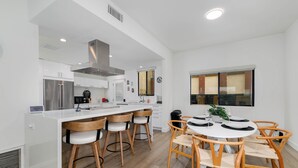 Une cuisine moderne avec des meubles blancs, un îlot central doté de tabourets et un coin repas avec des chaises en bois.