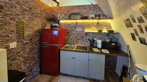 A compact kitchen with a stone wall, a red refrigerator, a sink, and a small countertop.