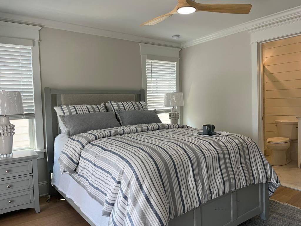 Une chambre à coucher comprenant un lit, des tables de chevet, une lampe, un ventilateur de plafond et une salle de bain avec des toilettes.