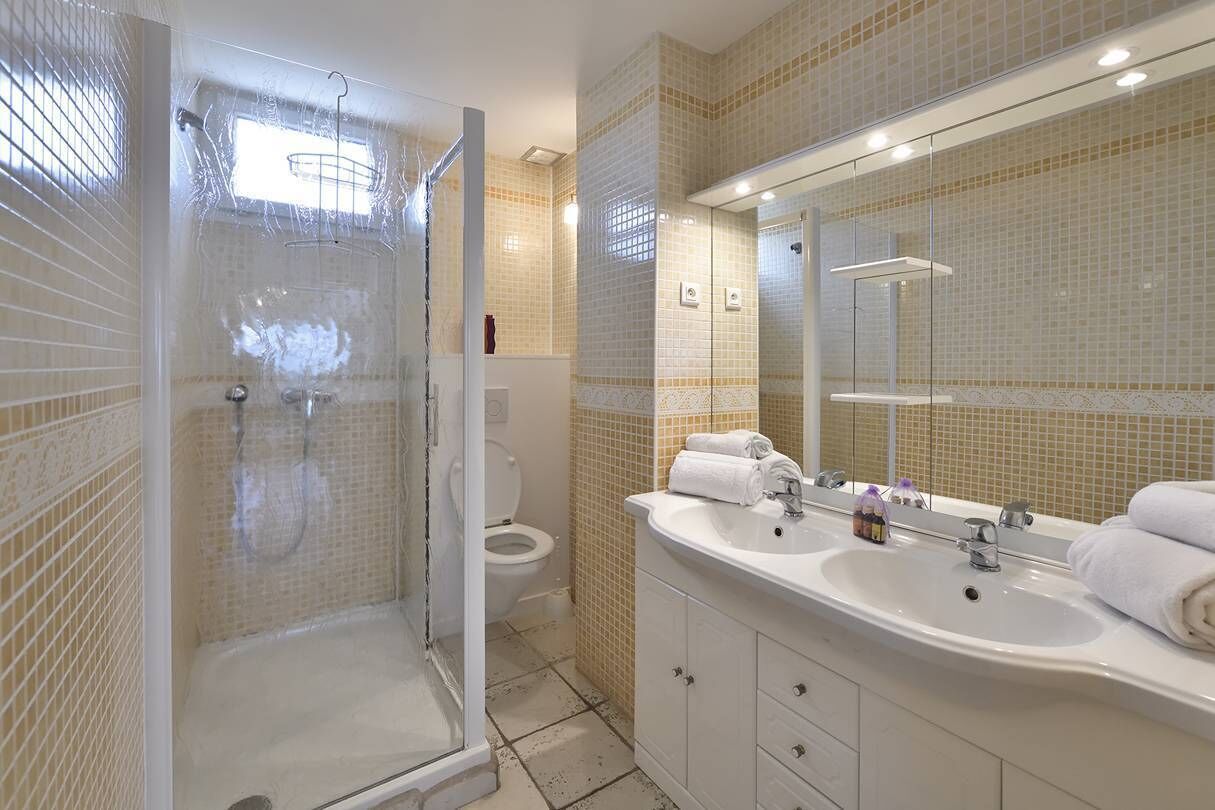 Un baño con cabina de ducha de vidrio, un lavabo blanco con dos espejos y un inodoro.