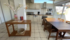 A kitchen with wooden cabinets, a dining table, chairs, and a view of the outside. - PAPRIKA - Villa Port Nature 69 - Luxury - 4 people (AGDE)