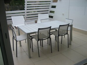 Eine Terrasse mit weißem Tisch und Stühlen, einem weißen Zaun und einem Fliesenboden.