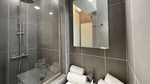 Un bany modern amb dutxa de vidre, un mirall gran i un lavabo blanc amb dues tovelloles.