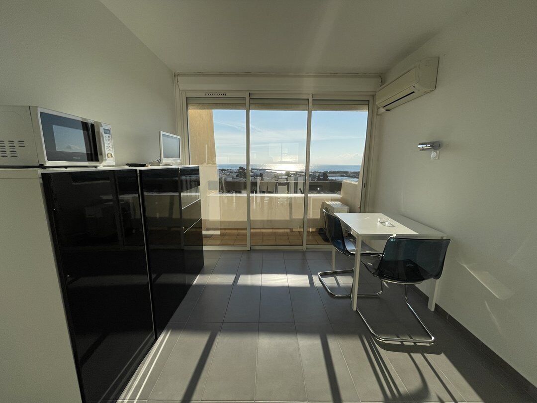 A compact kitchen with a microwave, toaster, and refrigerator, a balcony with a table and chairs, and a view of the cityscape.