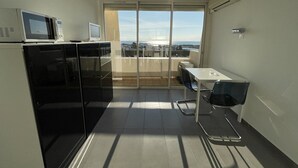 Cuina compacta amb microones, torradora i nevera, un balcó amb taula i cadires, i vista a la ciutat.