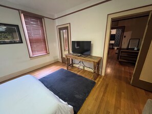 Una habitación con una cama, un televisor sobre una mesa de madera y una puerta que da a otra estancia.