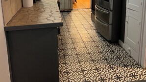 A kitchen with patterned flooring, a refrigerator, and cabinets.