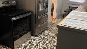A compact kitchen with a stainless steel refrigerator, a black stove, and patterned floor tiles.