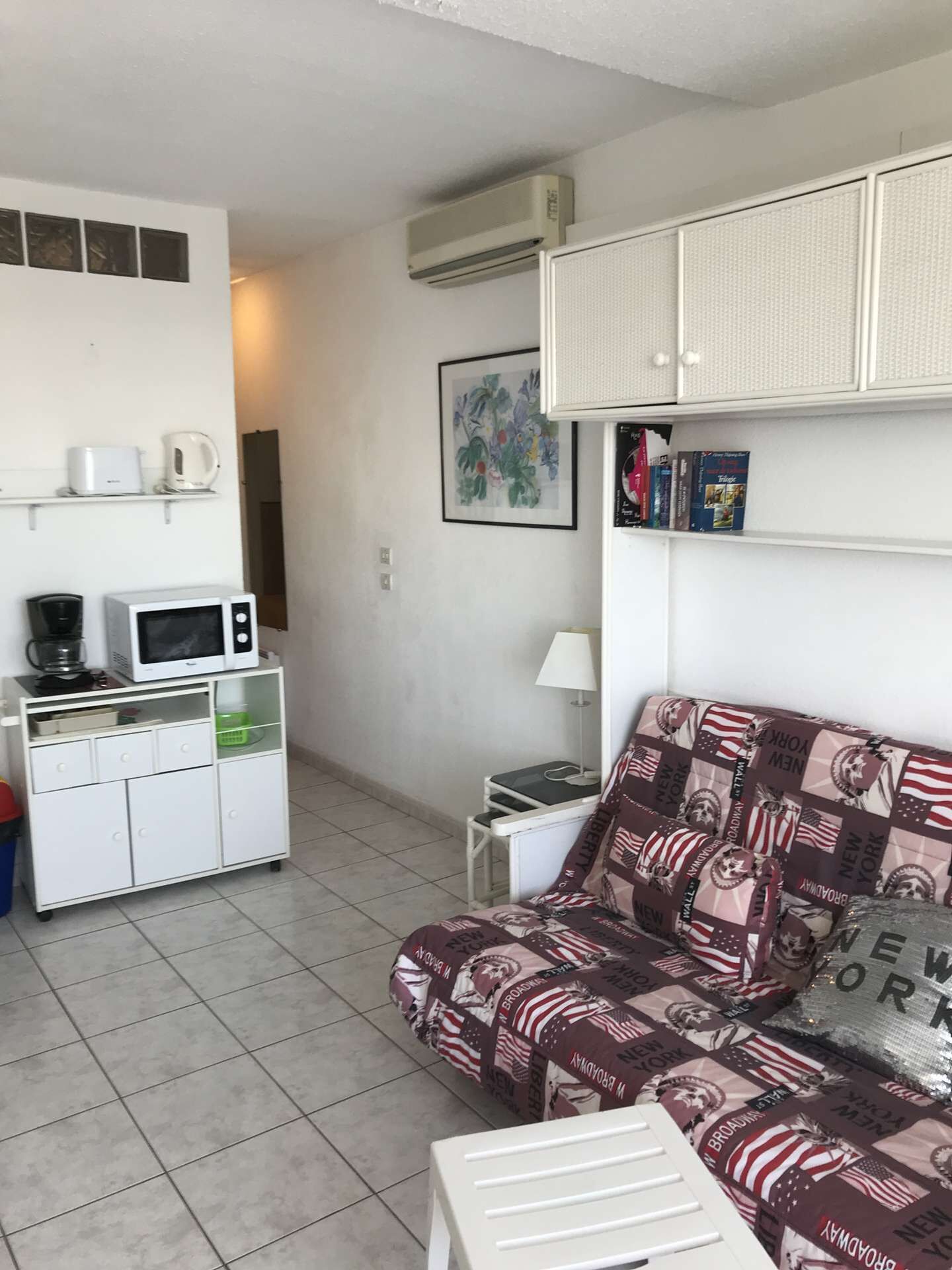 A compact living space with a kitchenette, a sofa with a Broadway-themed cover, a small table, and a wall-mounted air conditioner. - Port Nature Studio 627 - 3 people (AGDE)