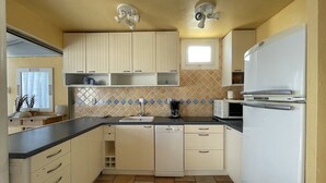 A compact kitchen with a dishwasher, a microwave, and a refrigerator. There are cabinets above the sink and a window above the countertop. - DUNE - Villa Port Nature 66 - Luxury - 4 people (AGDE)
