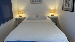 A single bed with a white and blue bedspread, two bedside lamps, a framed picture above the bed, and a wall-mounted lamp on the right. - DUNE - Villa Port Nature 66 - Luxury - 4 people (AGDE)