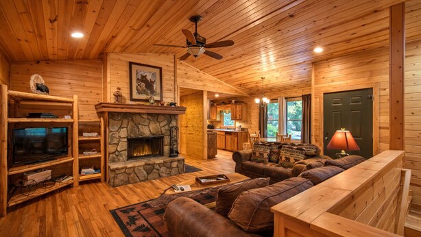 A log cabin interior with a stone fireplace, wooden furniture, a television, and a ceiling fan. - Bear Paw 1/1! Pool Table! Near Helen (Clarkesville)