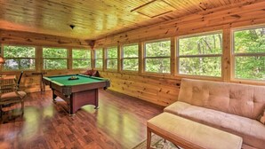 A wooden cabin interior with a pool table, a sofa, and large windows offering a view of the forest. - Bear Paw 1/1! Pool Table! Near Helen (Clarkesville)