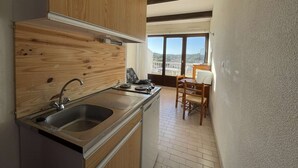 Cocina compacta con armarios de madera, un lavamanos y una estufa. Hay un comedor con mesa y sillas.