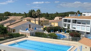 Una piscina con zona de sillones de sol, un espacio de descanso cubierto y vistas a edificios residenciales.