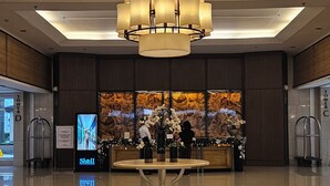A lobby with a large chandelier, a reception desk, and a digital screen displaying a corridor. - Shell Residences MOA - The Executive Suites SL004 1BR (Pasay City)