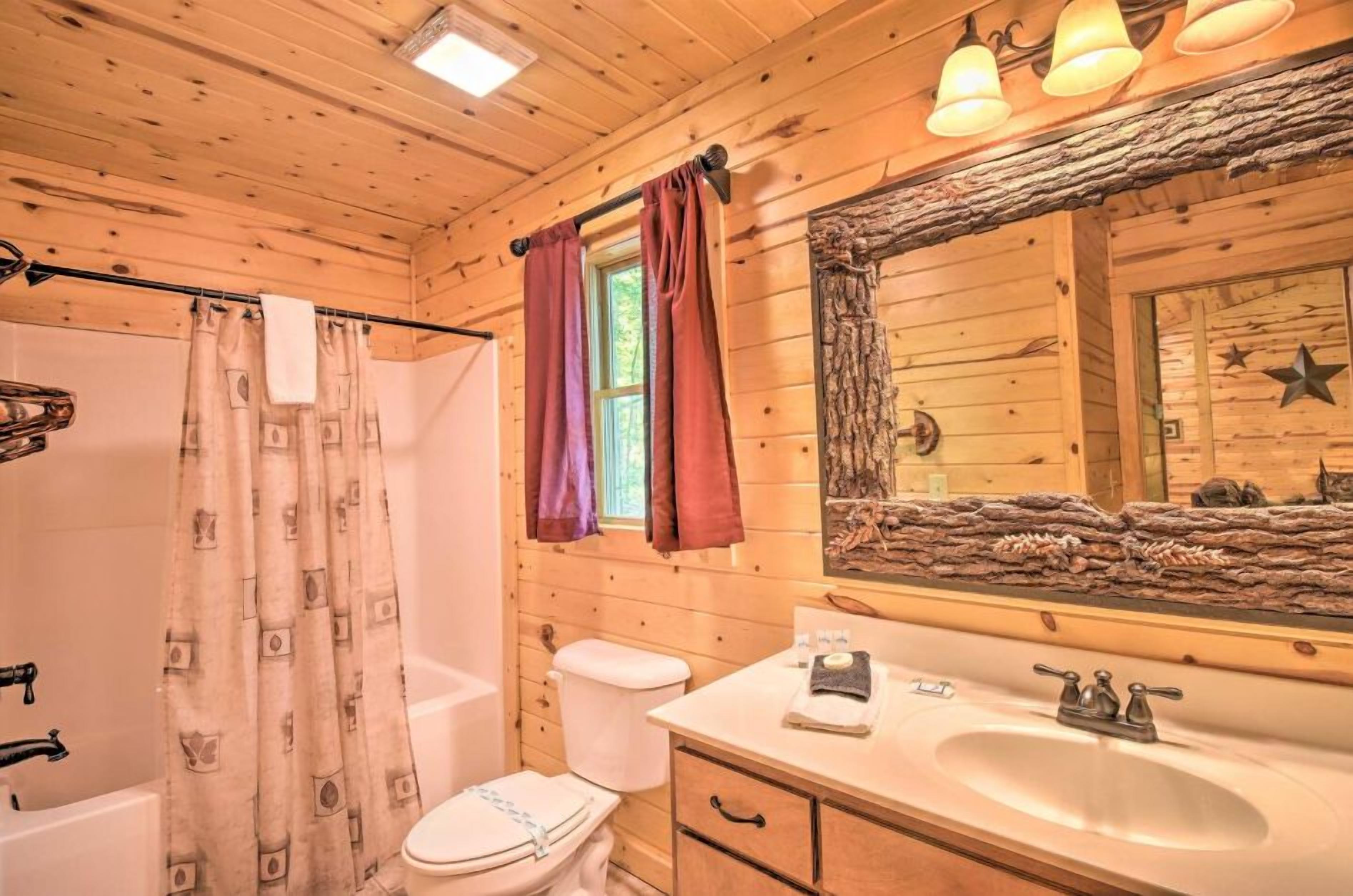 Une salle de bain rustique, aménagée dans une cabane en bois, avec une douche, des toilettes, un lavabo et un grand miroir.