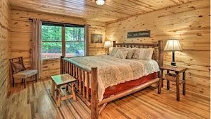 A log cabin room with a bed, a chair, a table, a window, and a sign on the wall. - Mountain Laurel 2/2! Pool table! Firepit! Close to Helen. (Clarkesville)