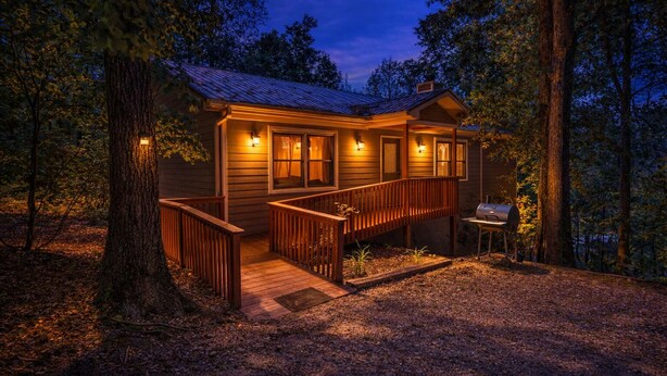 Eine Holzhütte mit einer Holzterrasse, einem Grill und einer Veranda mit Geländern.
