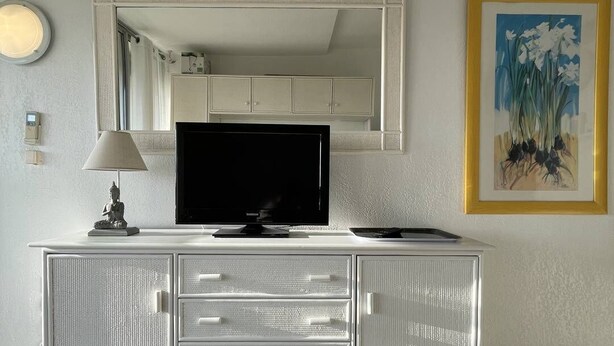 Ein modernes Zimmer mit einem weißen Schrank, einem Flachbildfernseher, einer Lampe und einem gerahmten Gemälde an der Wand.
