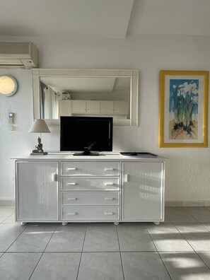 Ein modernes Zimmer mit einem weißen Schrank, einem Flachbildfernseher, einer Lampe und einem gerahmten Gemälde an der Wand.