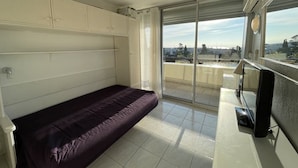 Ein Zimmer mit einem Bett, einem Fernseher, einer Glastür und Blick auf die Stadt.