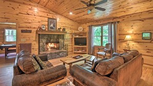 A log cabin interior with a stone fireplace, leather sofas, a television, and a ceiling fan. - Valley View 2/2! Pool Table! Near Helen! (Clarkesville)