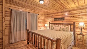 Camera da letto in una baita di legno, con un letto, tende, un comodino con una lampada e un cartello appeso al muro.