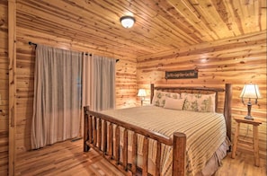A wooden cabin bedroom with a bed, curtains, a nightstand with a lamp, and a sign on the wall. - 2/1 Wishing Well with Pool Table! Minutes to Helen! (Clarkesville)