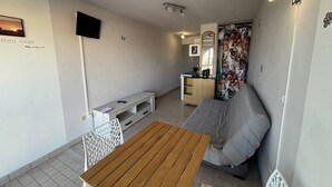 Ett kompakt bostadsutrymme med ett träbord, en soffa, en tv och ett litet kök.