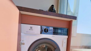 A compact, modern washing machine in a small, enclosed laundry area with a wooden floor and a window. - PINK LADY - Villa Port Nature 12 - Luxury - 4 people (AGDE)