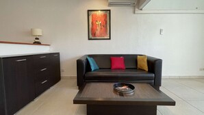 Ein modernes Wohnzimmer mit einer dunkelbraunen Ledersofa, einem Couchtisch, einem Bild an der Wand und einer Küchenzeile mit Schränken und einer Lampe.