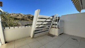 Ein durch eine Mauer geschützte Terrasse mit Fliesenboden und Blick auf eine angelegte Hügelanlage.