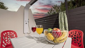 Een tafel met twee glazen rode en oranje drankjes, een fruitmand en rode stoelen.