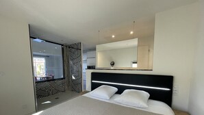 Een moderne hotelkamer met een groot bed, een nachtkastje, een spiegel boven het bed en uitzicht op het interieur van de kamer.