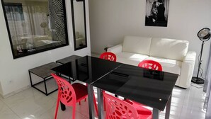 Een moderne woonkamer met een eethoek, een witte bank en een zwarte eettafel met rode stoelen.