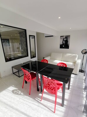 A modern living room with a dining area, a white sofa, and a black dining table with red chairs. - SWING – Villa Port Nature 50 – Luxury – 2 People (AGDE)