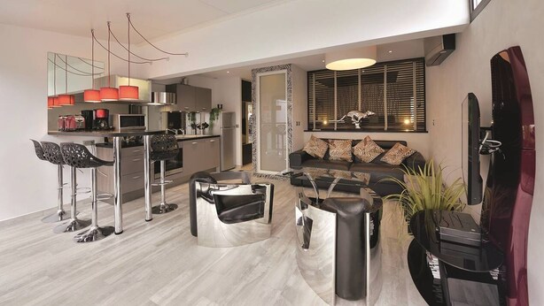 A modern living room with a sofa, coffee table, and bar stools. There is a kitchen area with appliances and a dining table. - VILLA SAVANNAH - Villa Port Nature 105 - Luxury - 4 people (AGDE)