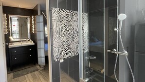 A modern bathroom with a glass shower enclosure, a vanity with a mirror, and a dark tiled floor. - VILLA SAVANNAH - Villa Port Nature 105 - Luxury - 4 people (AGDE)