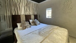 A bedroom with a large bed, a headboard with a textured design, a small window, and a motivational wall quote. - VILLA SAVANNAH - Villa Port Nature 105 - Luxury - 4 people (AGDE)