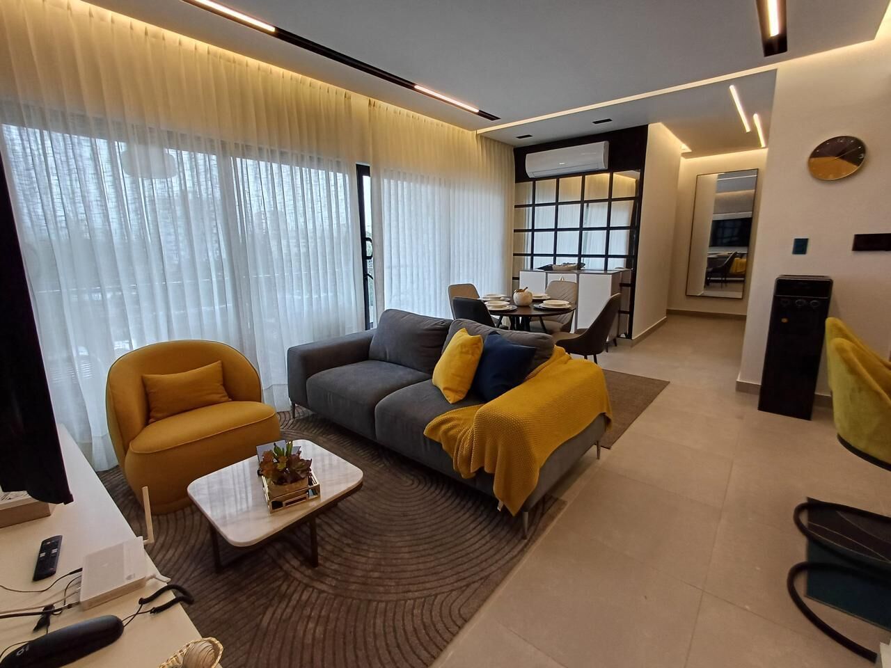 A modern living room with a sofa, armchair, coffee table, and a dining area in the background.